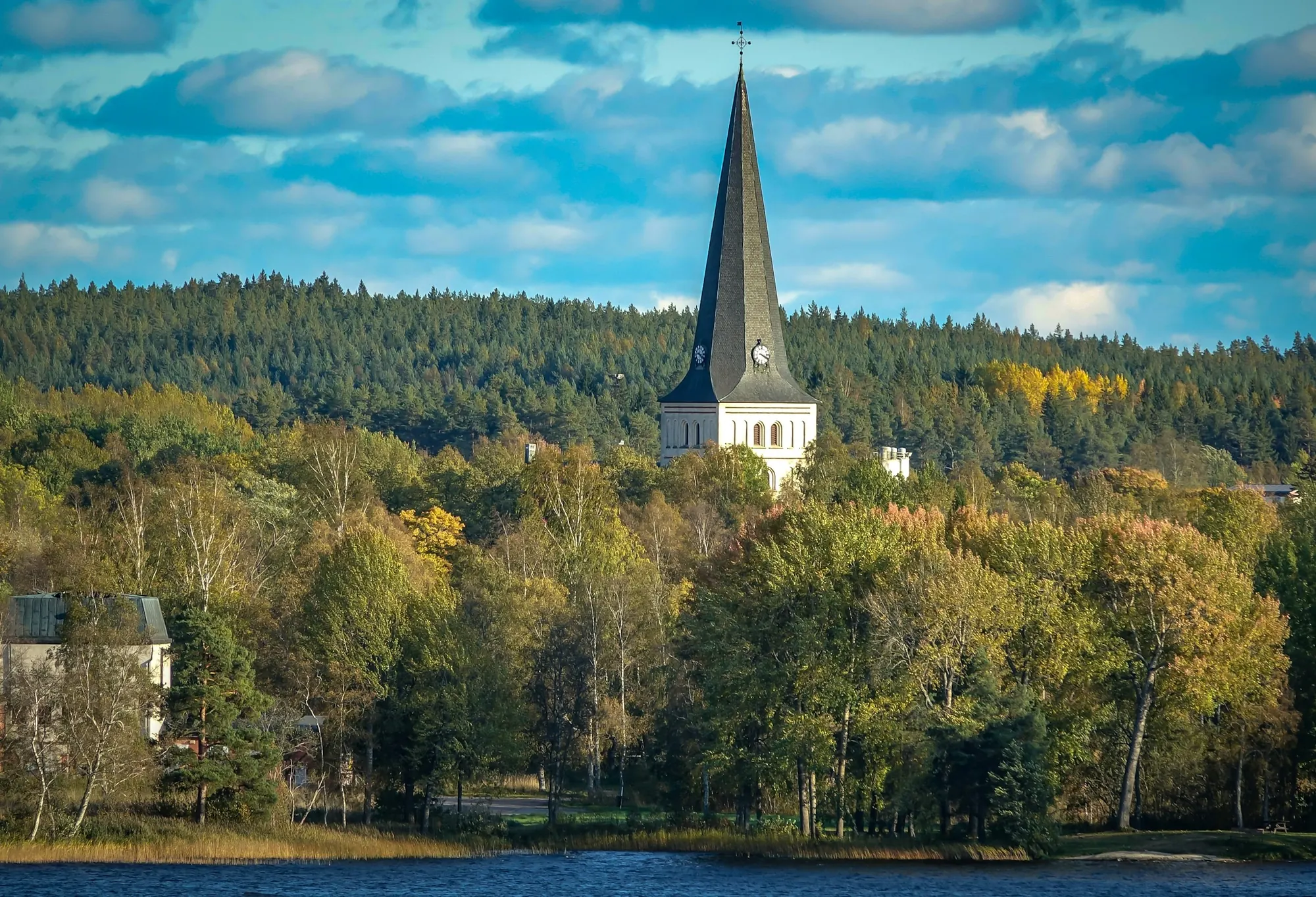 Kyrktorn över höstskog vid en sjö